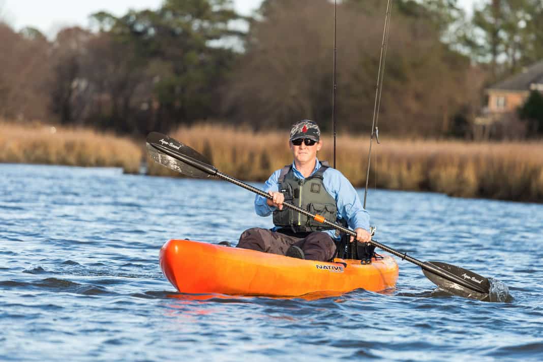 man paddling an orange native watercraft fishing kayak