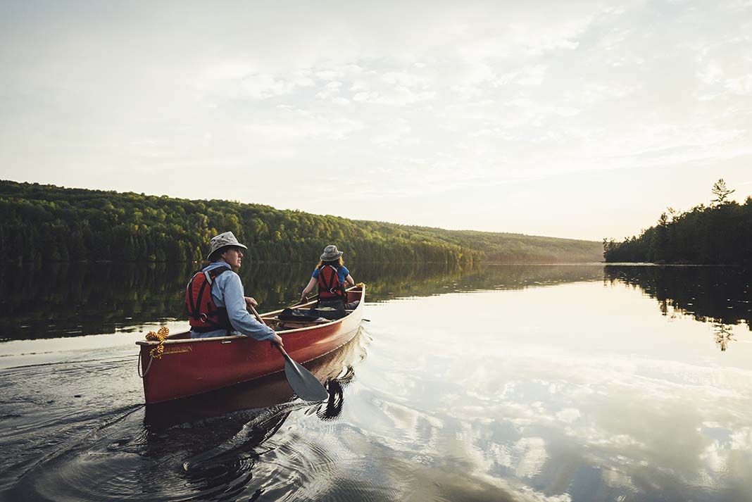 A couple paddles a red canoe across a lake in Algonquin Park