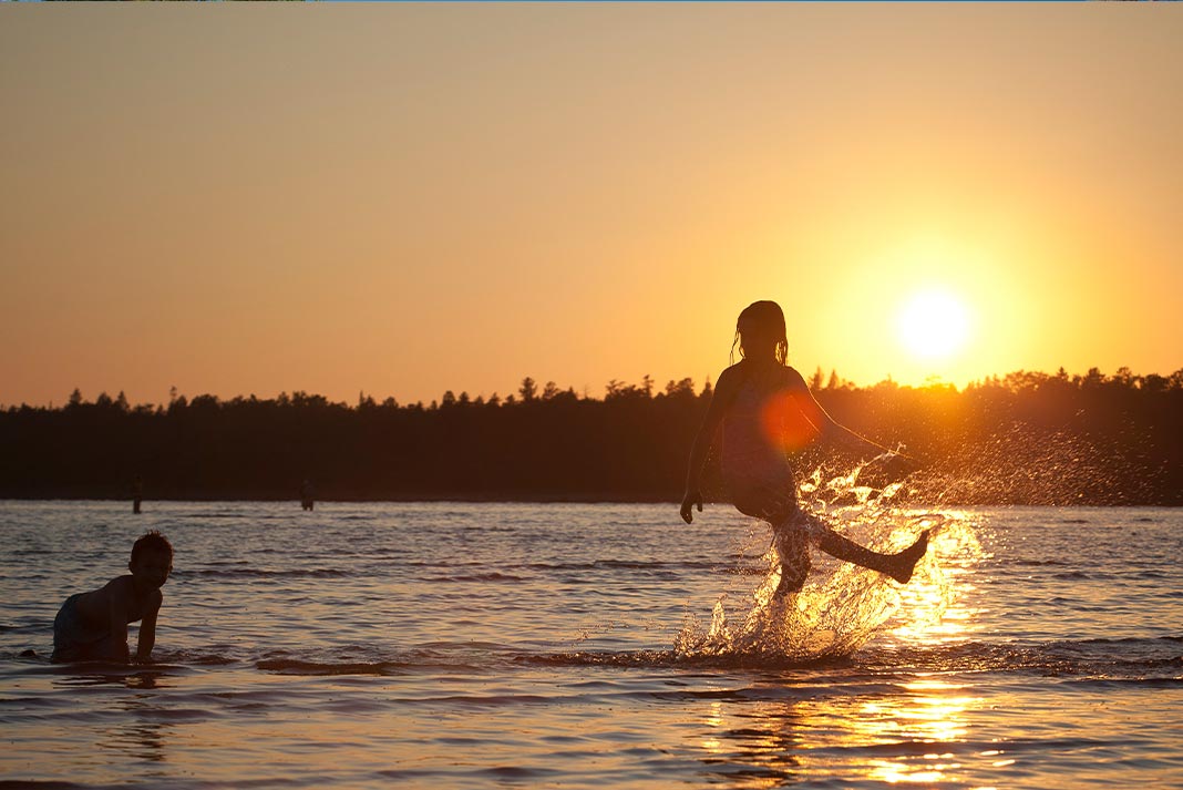 Two kids playing in the water at sunset
