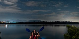 Girls kayaking on a bioluminescent bay under a cloudy night sky