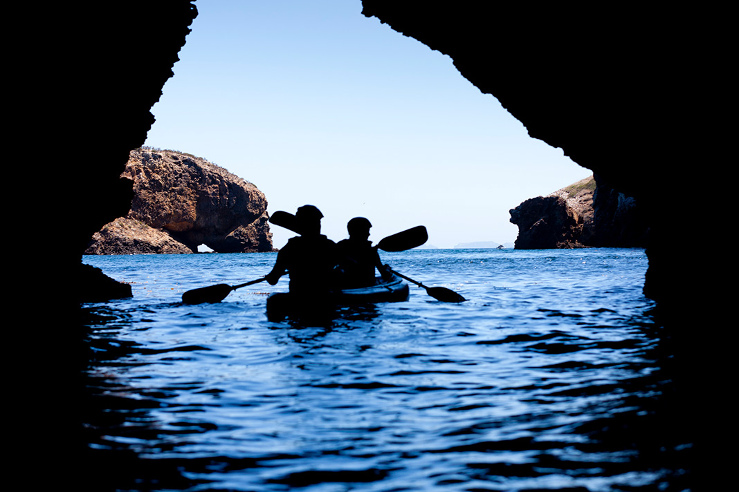 Kayakers paddling through a cave in blue waters