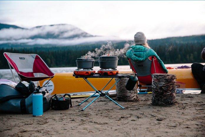 Person sitting in camp chair on the sand with canoe beached in front of them.