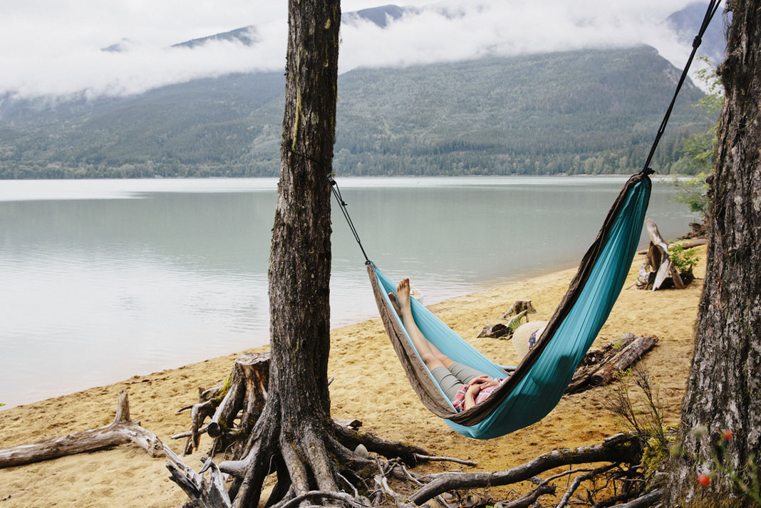 Person lying in hammock on a beach with mountain in background.