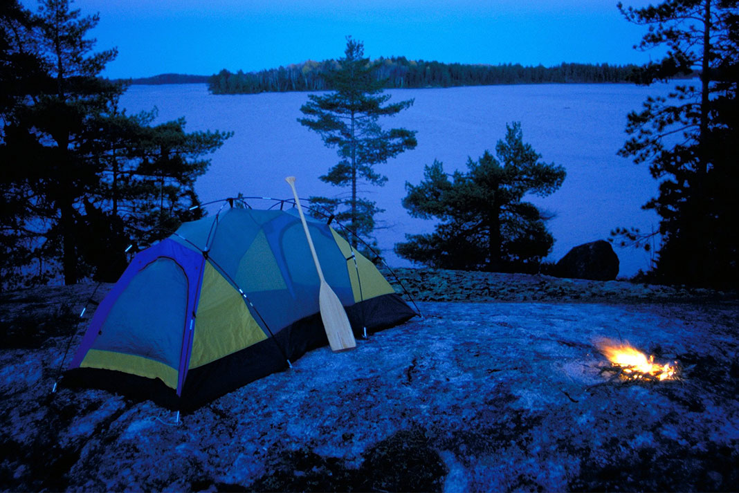 Tent set up on a rock while a campfire burns at night