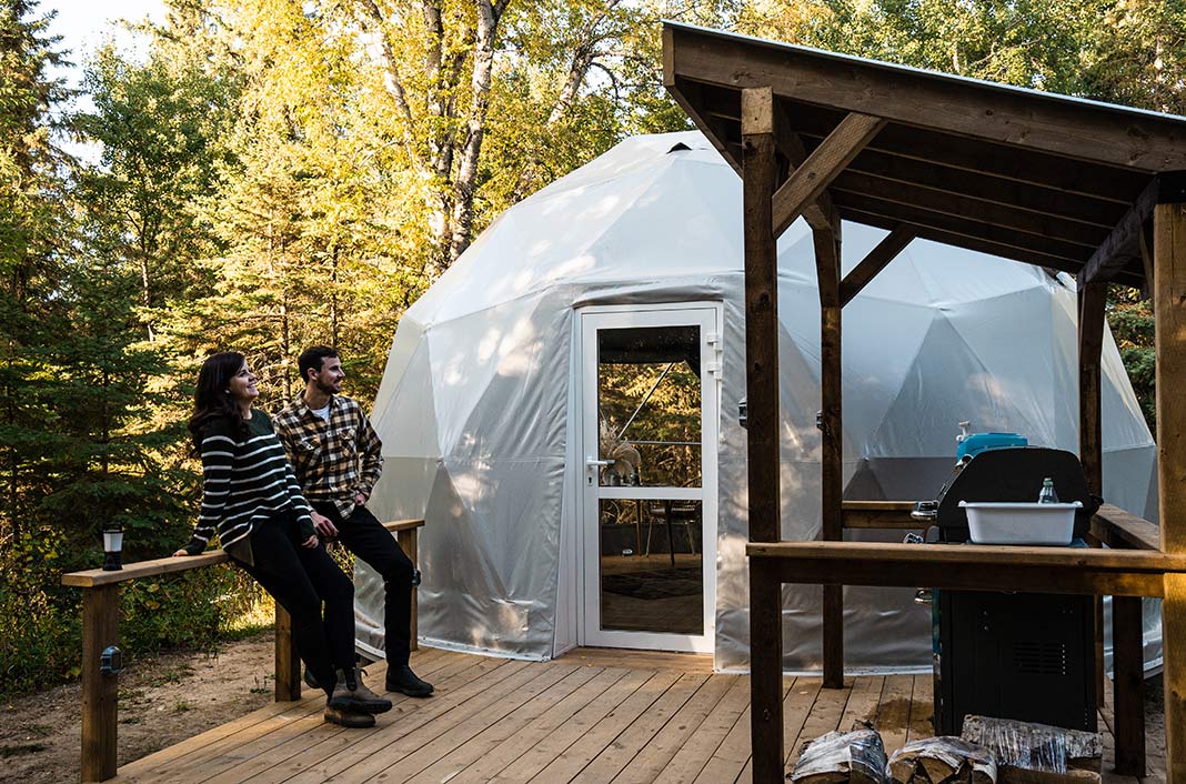 People sit outside on the deck of a geodome while camping near Edmonton