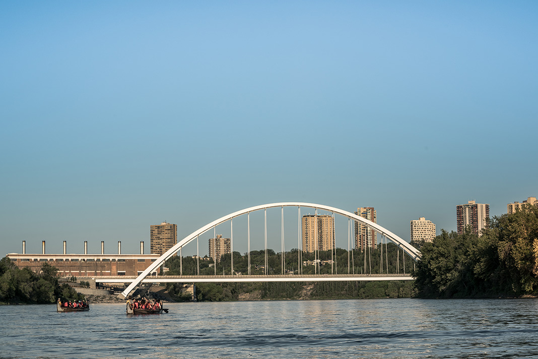 A tour group paddles in voyageur boats past the Walterdale Bridge