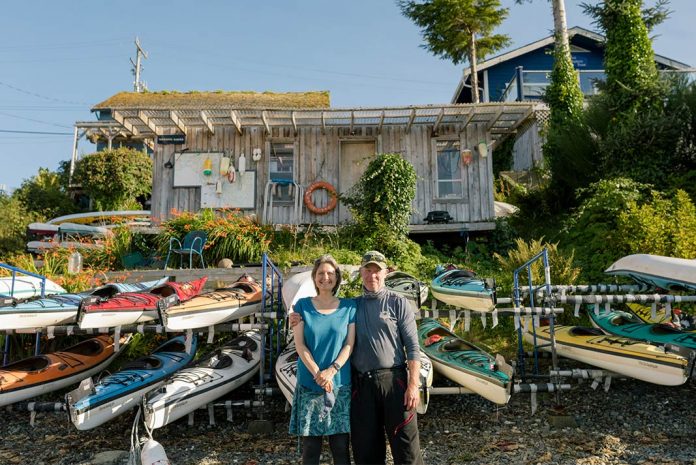 A couple stands in front of several kayaks
