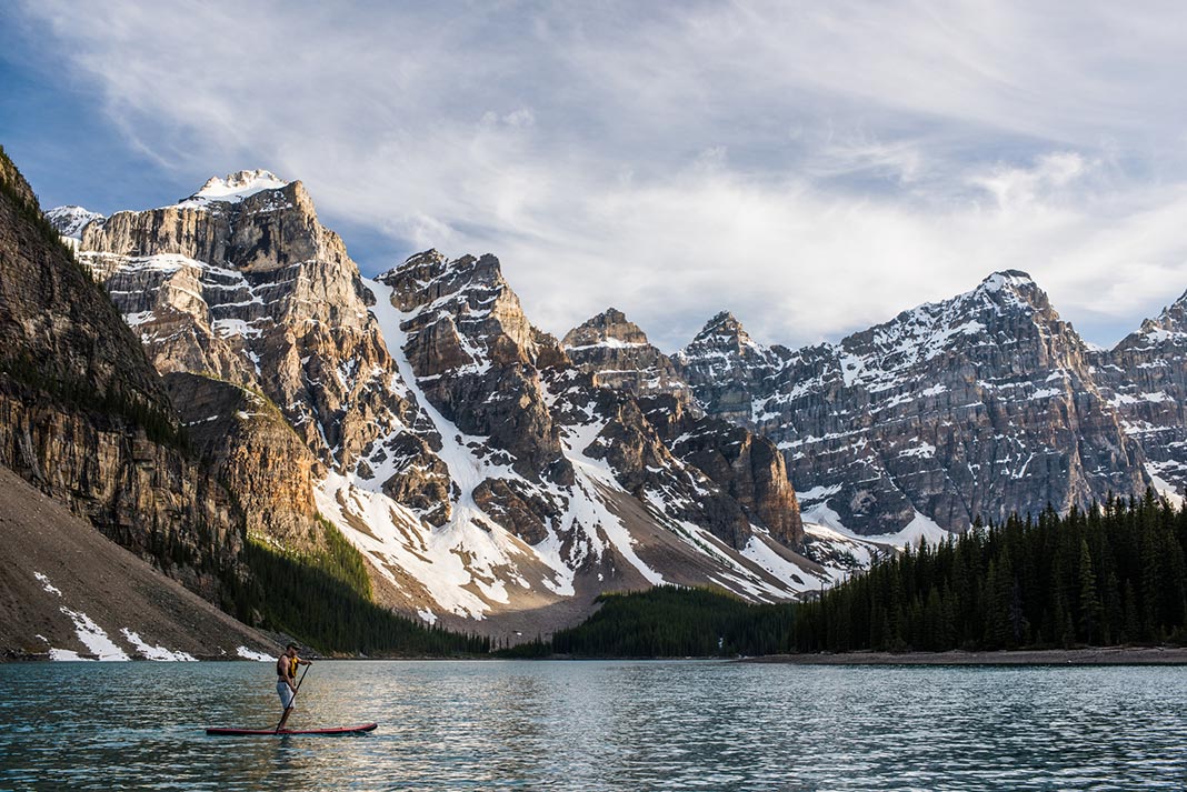 A standup paddleboarder on Moraine Lake, snowcapped mountains in the background