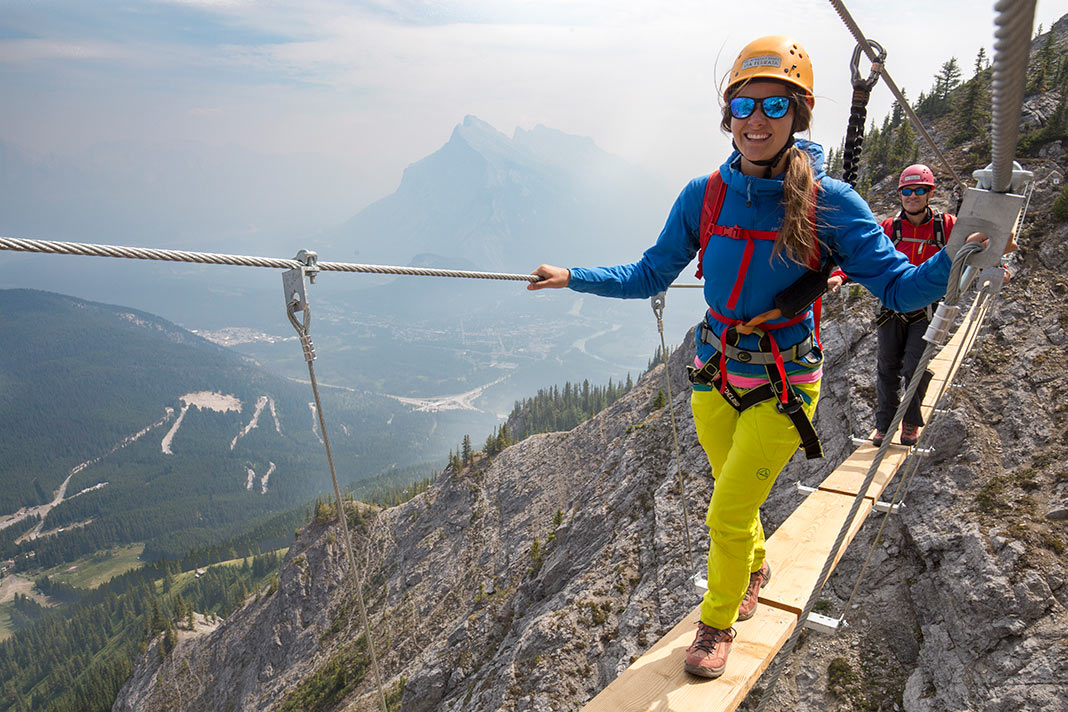 A rock climber walks on a plank bridge overlooking the mountains