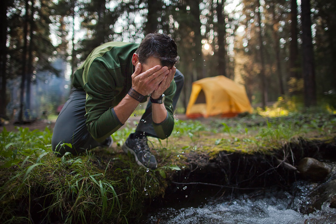 Man washing his face in stream next to campsite
