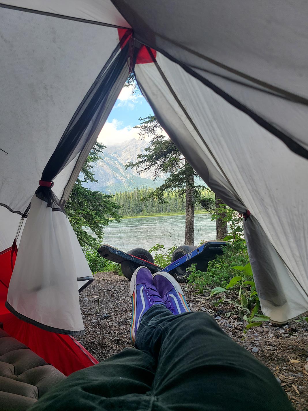 View of someone's legs sticking out of tent opening with lake and mountains in background