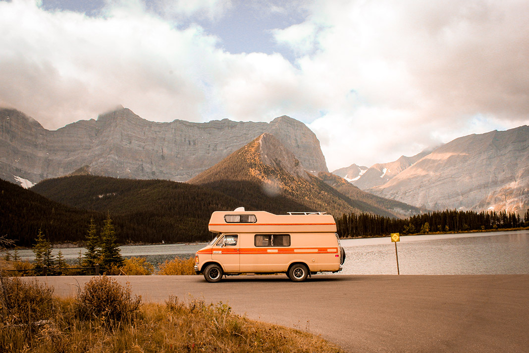 Camper van parked at side of the road in front of a lake and mountains.