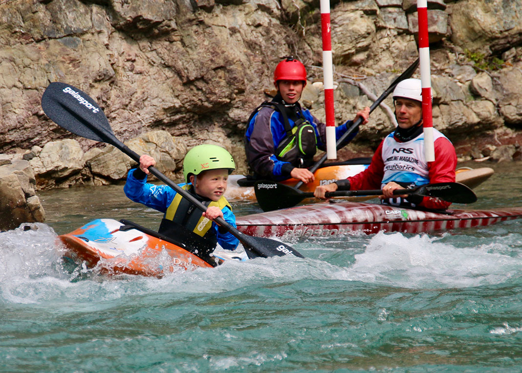 Child kayaking through slalom gates on a river with two adults in background