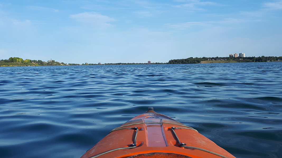 Front of kayak on a lake with buildings and shore in background