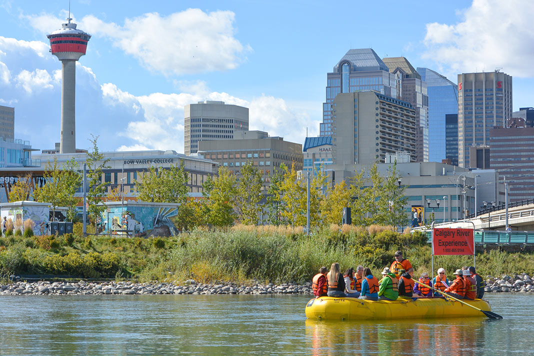 People in yellow raft on river with Calgary buildings in background.