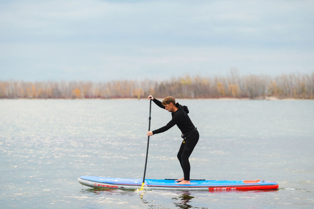 Man wearing wetsuit and paddling on paddleboard.