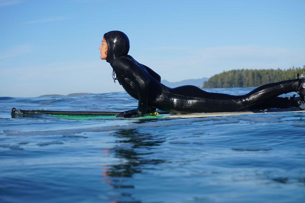 Woman wearing wetsuit and lying on paddleboard on the water.