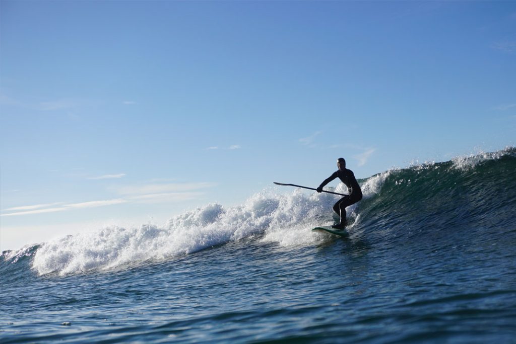 Person surfing a wave on a paddleboard, paddle in hand