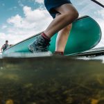 Ultimate Guide To Choosing The Best Shoes For Canoeing Person wearing hiking boots walking beside front of canoe in the water.