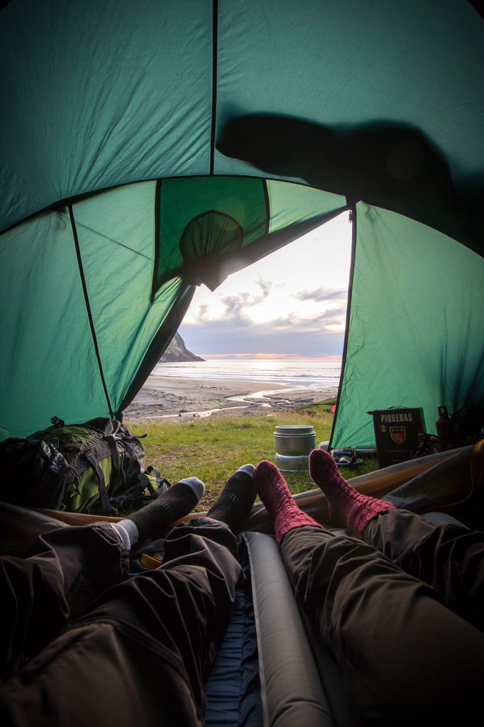 Two people wearing wool socks with open tent revealing view of the water.