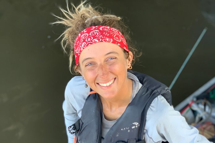Woman wearing bandana and PFD, standing on a rowboat.