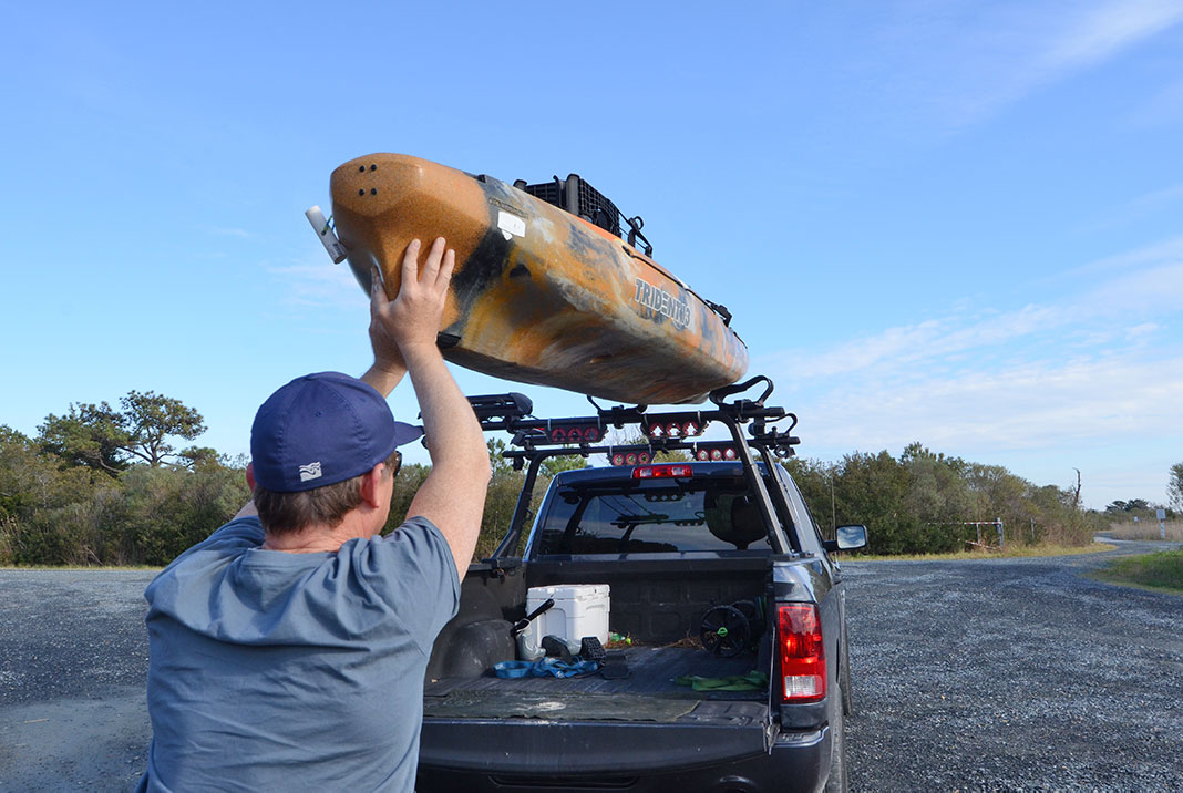 man loads his fishing kayak onto a roof rack for transport