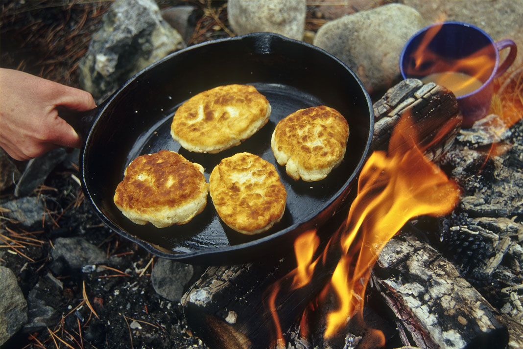 Pan of bannock being held over a fire.