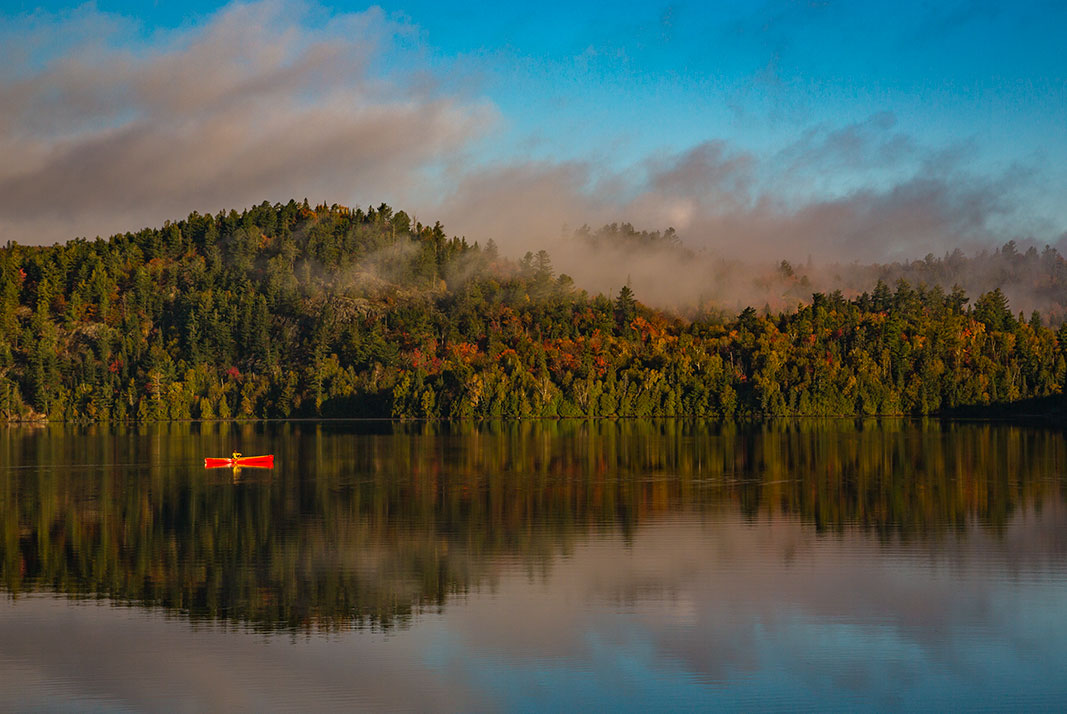 Red canoe on lake with tree-covered hill in background and mist.
