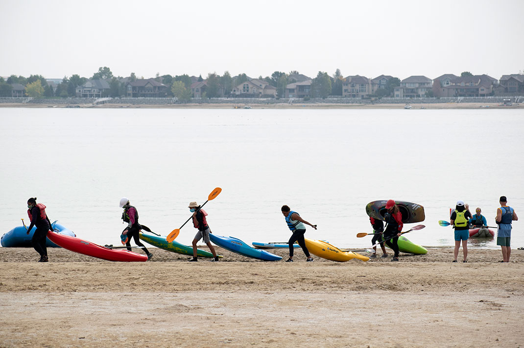 Paddlers dragging kayaks in a line along the beach.