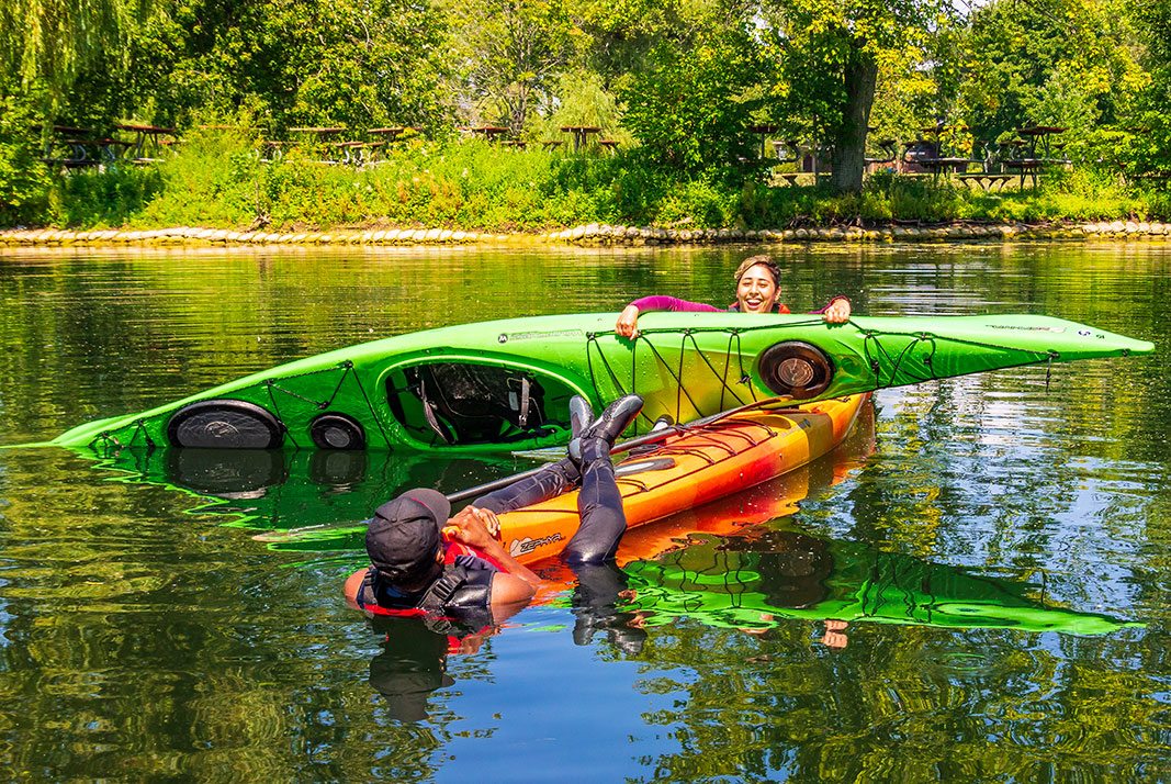 Two people performing a kayak over kayak rescue.