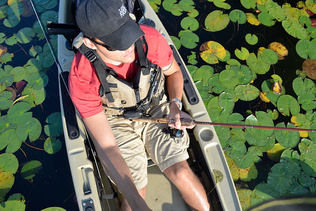 Man floats among lily pads and fishes from a hybrid fishing kayak
