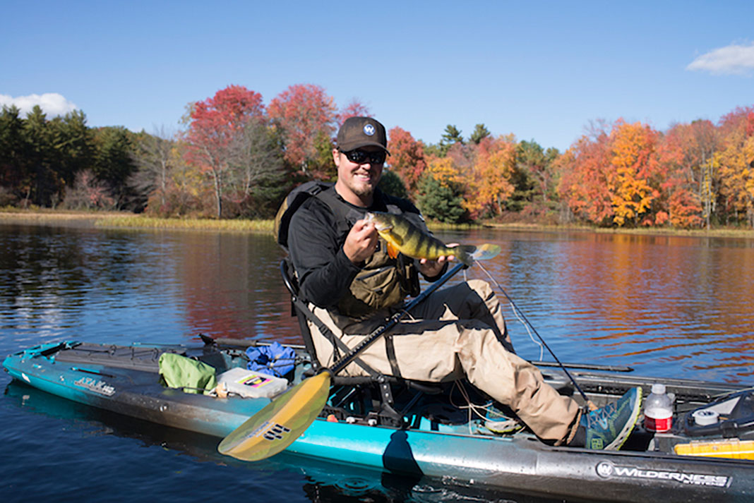 kayak angler grabs his fish and grins on a fall lake
