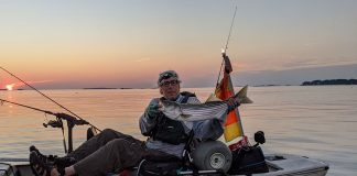 kayak angler holds up striped bass caught with tube and worm rig
