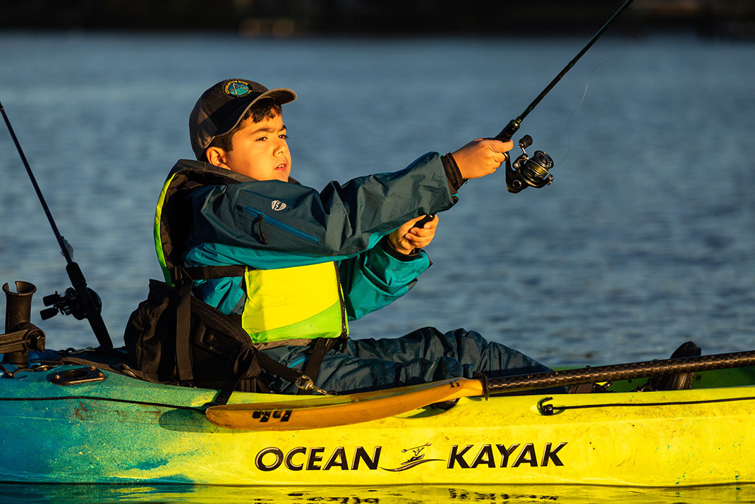 A boy casts his kids fishing rod from an Ocean Kayak outfitted with fishing gear