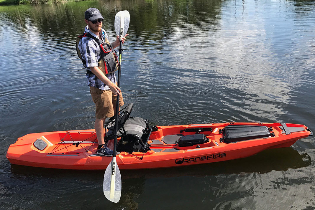 Man stands with paddle on top of the Bonafide SS127 fishing kayak