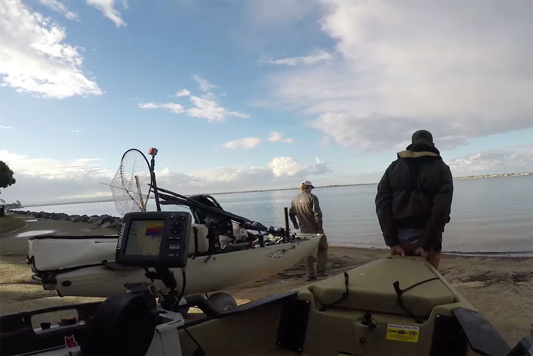 two men wheel their Hobie Pro Angler 14 fishing kayaks to the water
