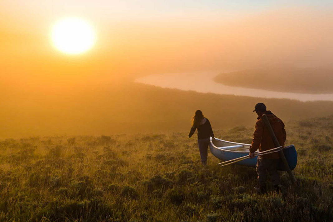Two paddlers carry a canoe in the dawn light, building healthy relationships through paddling