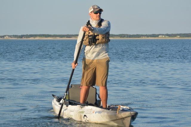 man stands on a kayak and paddles with a SUP paddle while sight fishing
