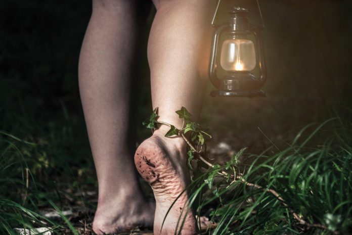 Woman walking barefoot through grass holding lantern