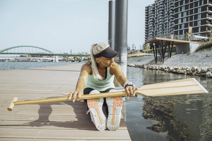 Woman stretching with a canoe paddle on a dock