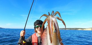 man on fishing kayak holds up a giant squid he caught