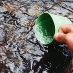 4 Ways Of Treating Water In the Backcountry To Make It Safe To Drink Person scooping up water using a green cup | Photo by Jens Johnsson from Pexels