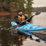 101 Things Every Paddler Should Know Man wearing hat, drysuit, gloves and PFD paddling blue touring kayak