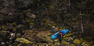 Man carrying whitewater kayaks as stands on boulders.