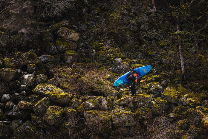 Man carrying whitewater kayaks as stands on boulders.