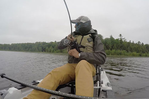 man sets the hook in a fish on a kayak in cool weather