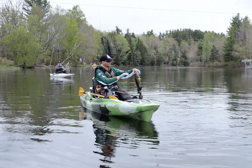 man holds up fish from a fishing kayak