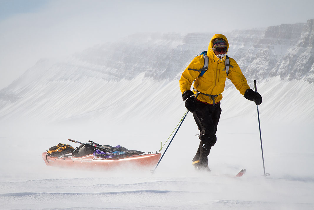 Man on skis towing a sea kayak through the snow.