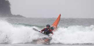 Woman smiling as her sea kayak plunges into the surf