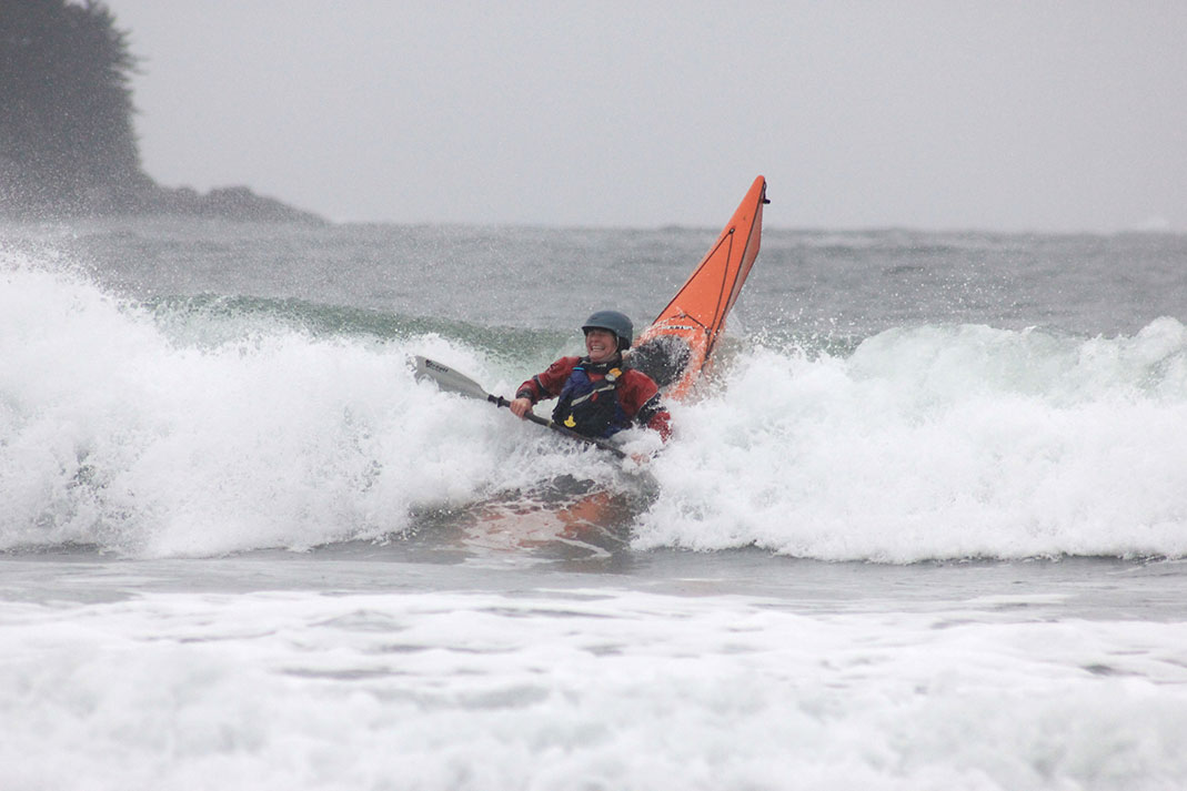 Woman smiling as her sea kayak plunges into the surf